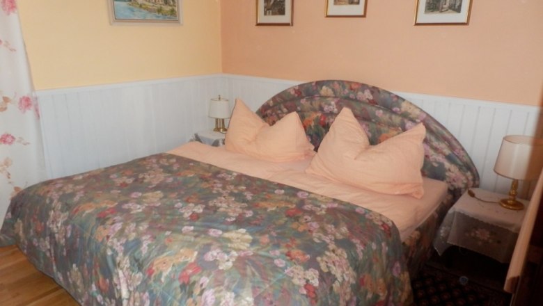 Bedroom with double bed, floral bed linen and pictures on the wall.