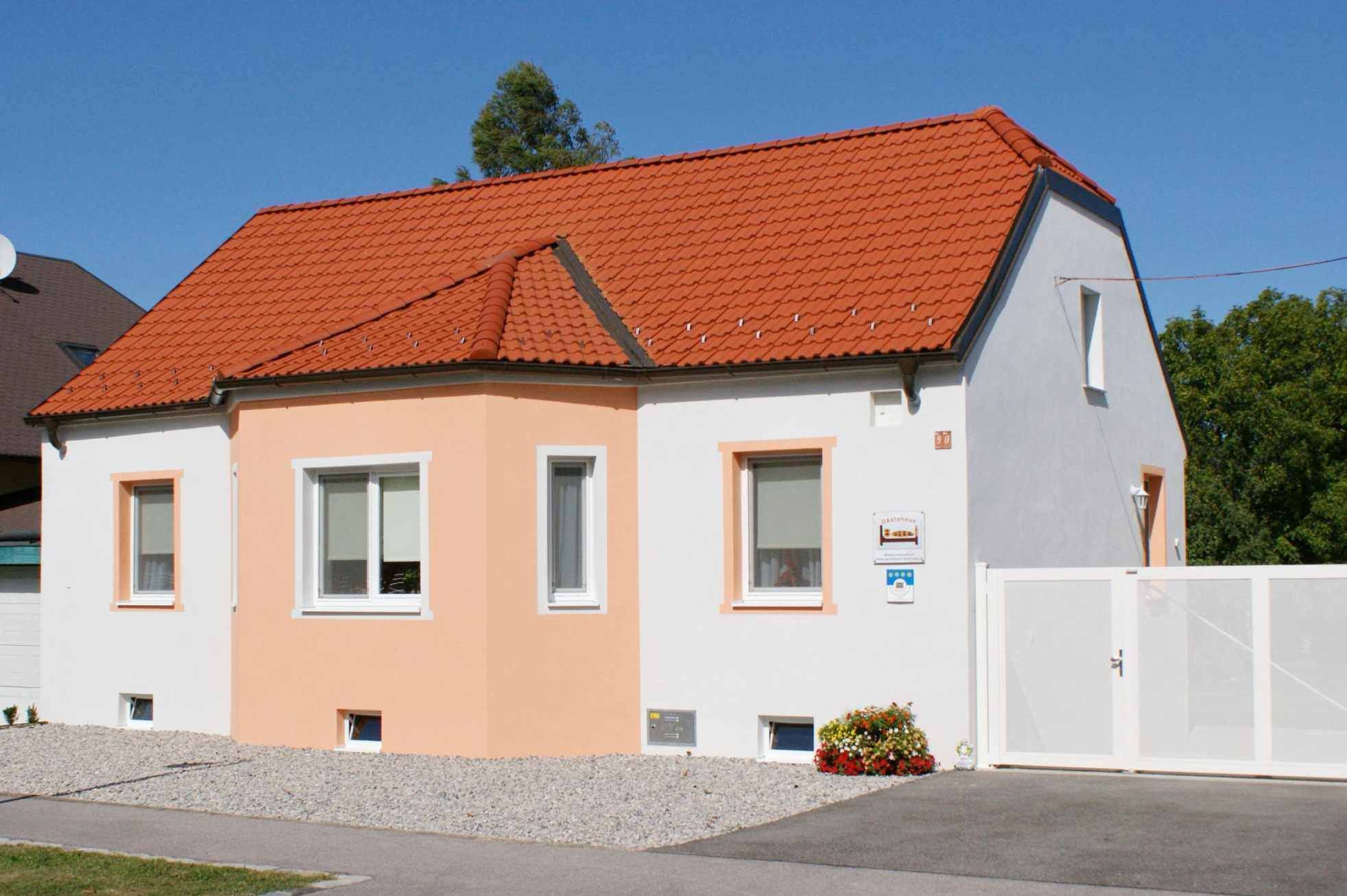 A small, single-storey house with an orange roof and white façade under a blue sky.