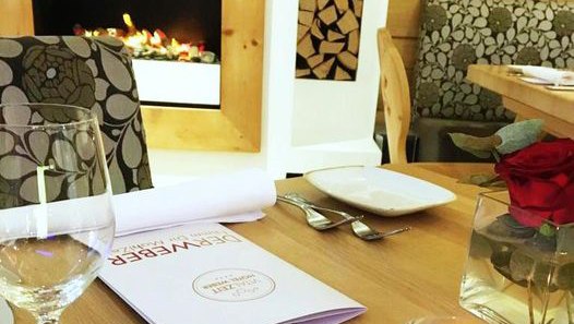 Interior view of a restaurant with table setting, wine glass, menu and fireplace.