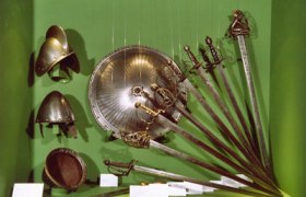 Exhibition of antique weapons and helmets in a green display case.