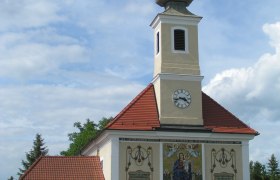 Maria Ellend pilgrimage church with tower and clock, decorated with religious motifs.