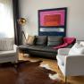 Modern living room with leather sofa, two white armchairs, floor lamp and abstract painting on the wall.