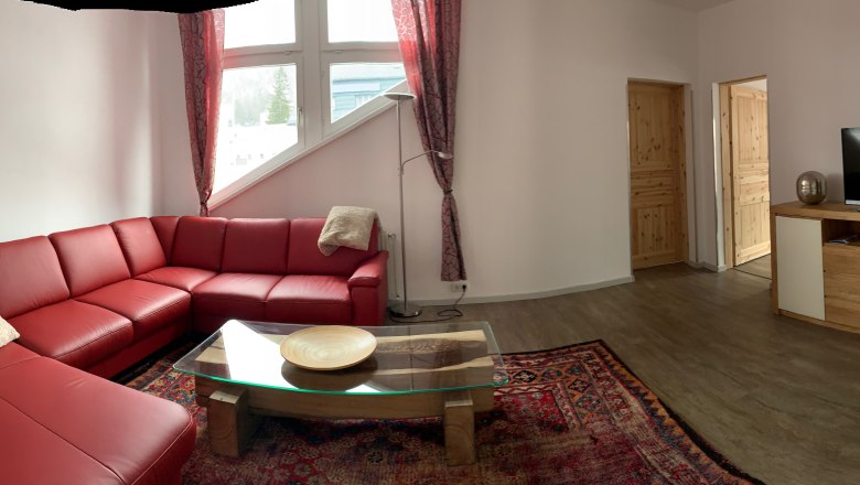 Living room with red leather sofa, glass table, carpet and TV on wooden cabinet.