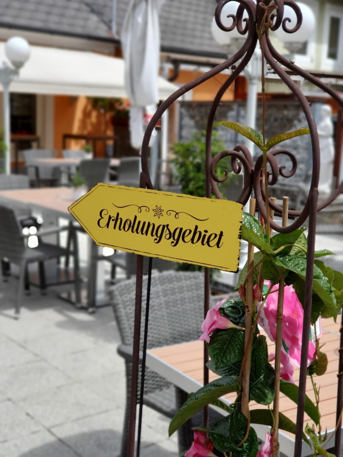 A sign saying 'Recreation area' in a café garden with tables and chairs.