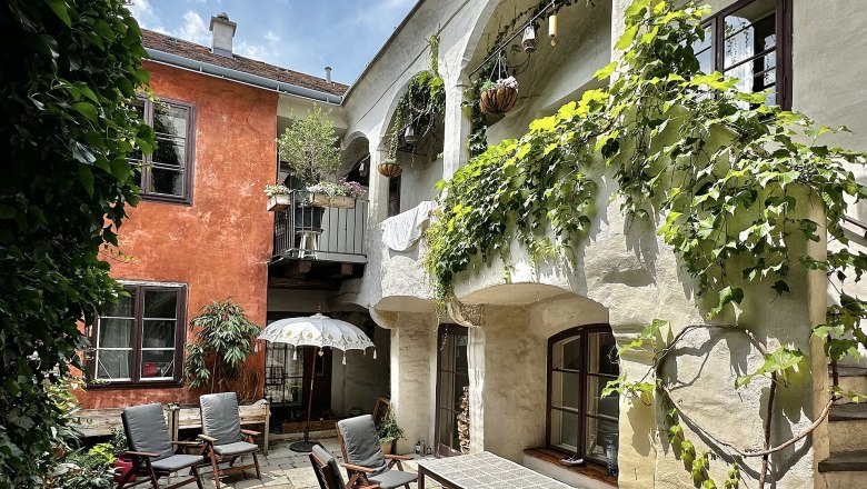 A cozy courtyard with plants, wooden furniture and a parasol.