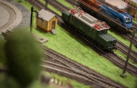 Model railroad with green train and small building on a layout.