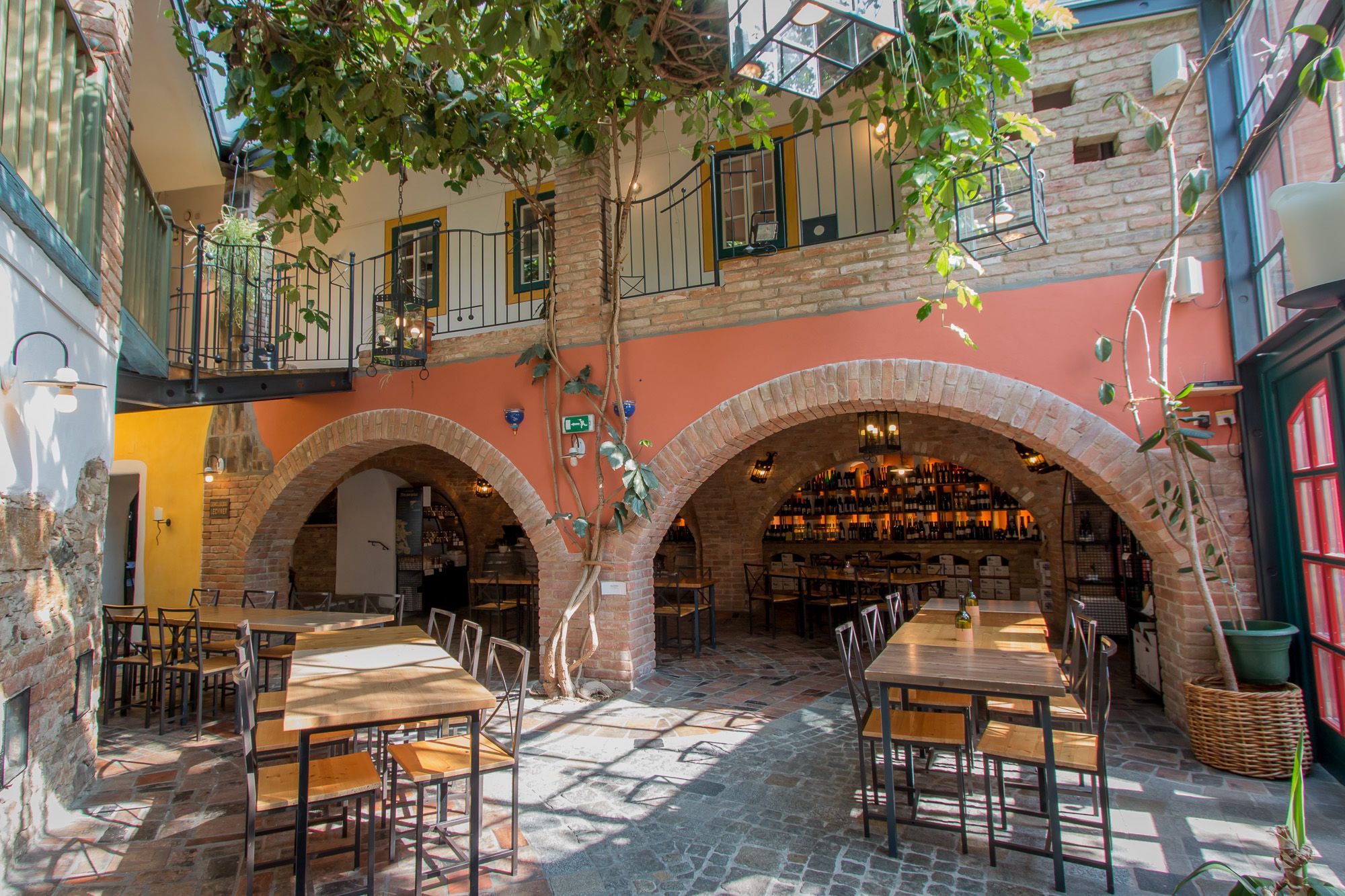 Inner courtyard of a restaurant with tables, chairs and plants, surrounded by brick arches and a balcony.