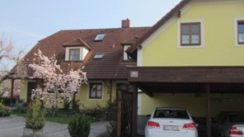 Yellow guest house with flowering tree and two parked cars.