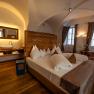 Comfortable hotel room with double bed, wooden wall, washbasin and desk in front of two windows.