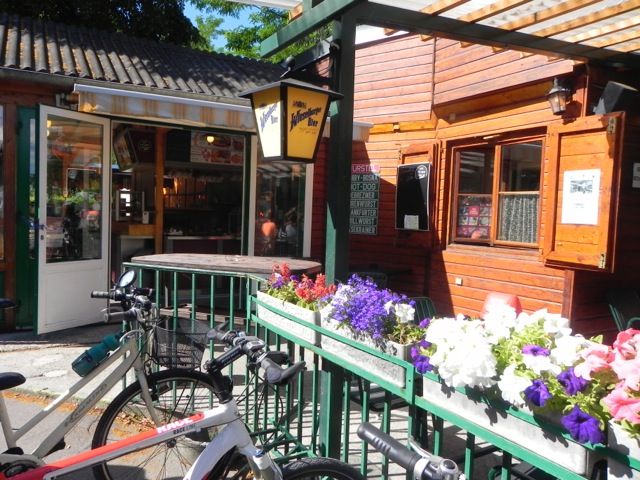 A cozy snack bar with wooden walls, bicycles and blooming flowers in the foreground.
