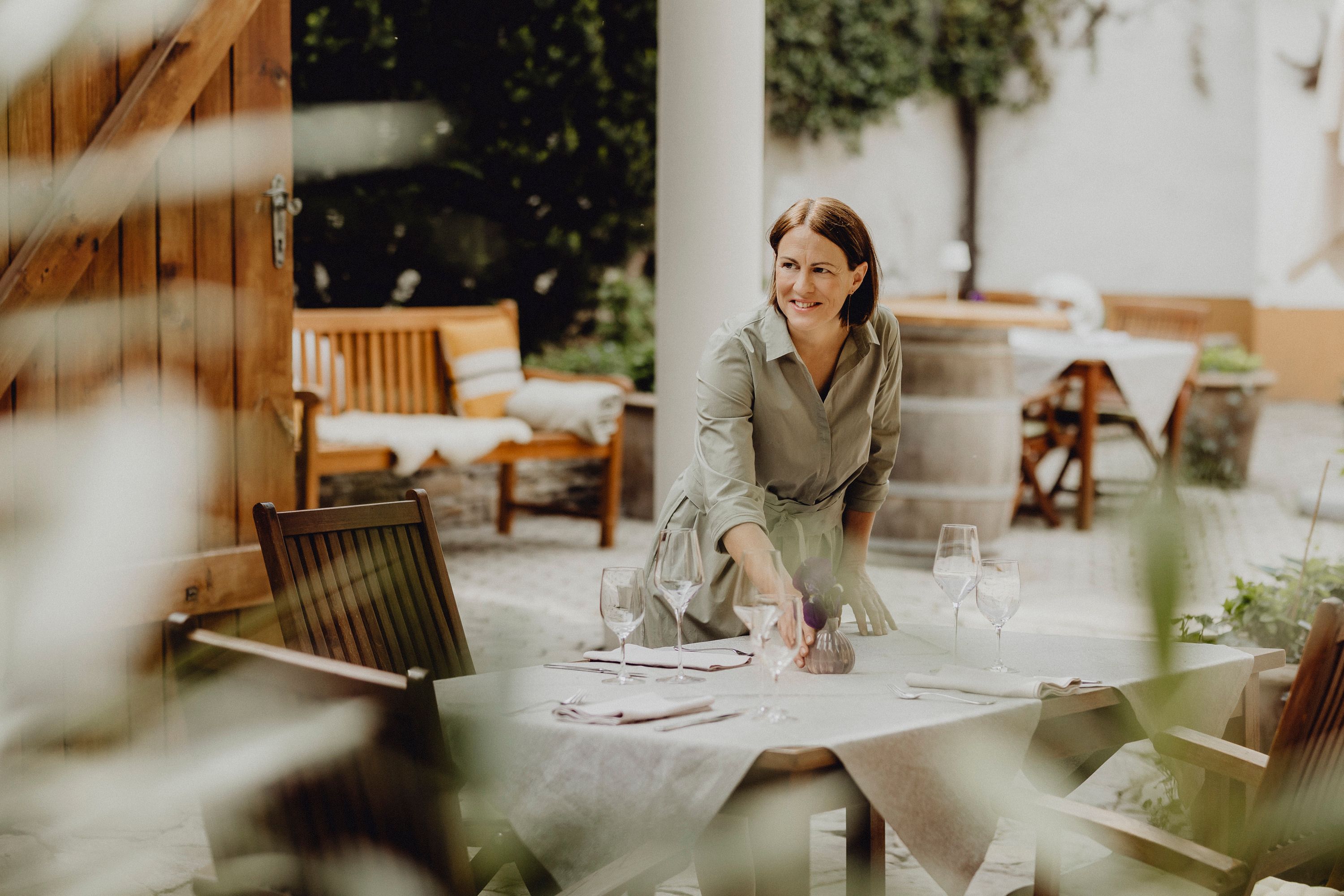 Woman sets table outdoors with wine glasses and napkins.