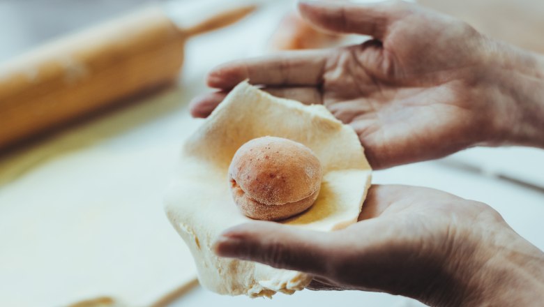 Hands form a dough around an apricot.