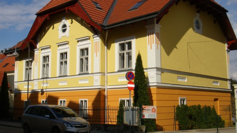 Yellow and orange building with a red roof and a parked car in front of it.