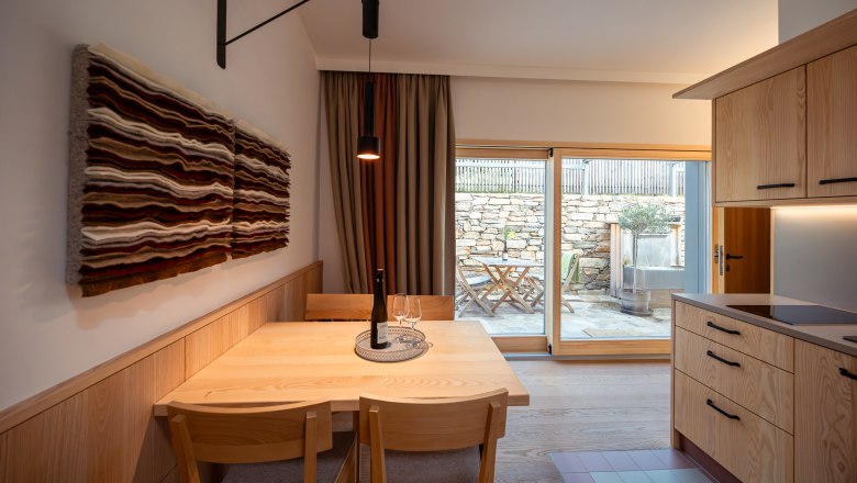 Interior view of a modern dining area with wooden furniture and wall art, view of a terrace through a glass door.