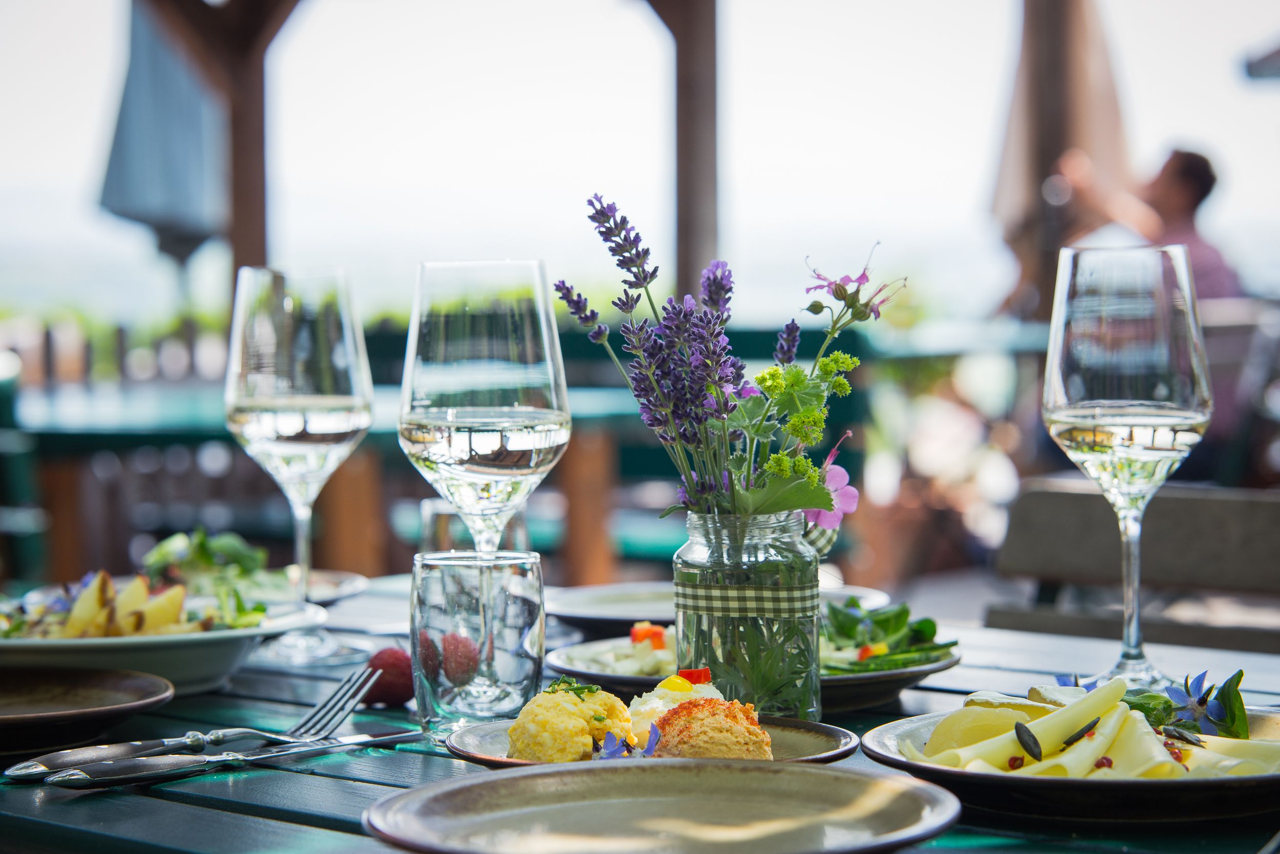 A table set outside with wine glasses, flowers and food.