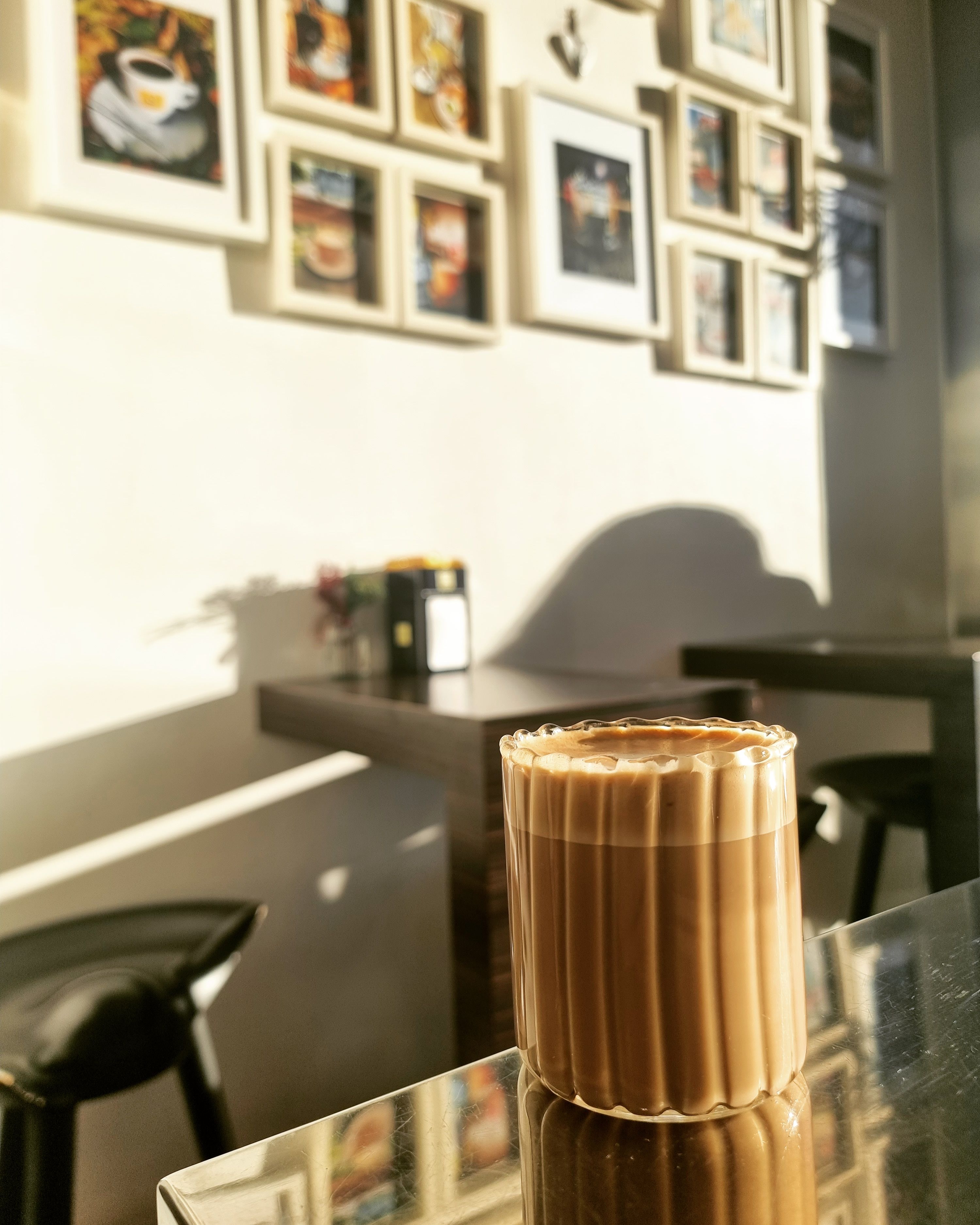 A glass of coffee on a table in a café with a picture frame on the wall in the background.