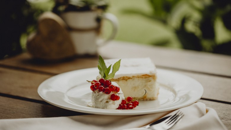 A plate with a cream slice, cream, red currants and a mint leaf on a wooden table.