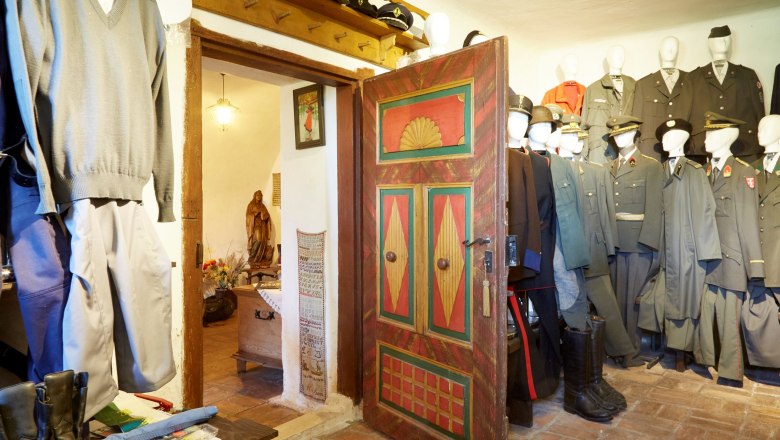 Interior view of a room with old uniforms and a colorfully painted wooden door.