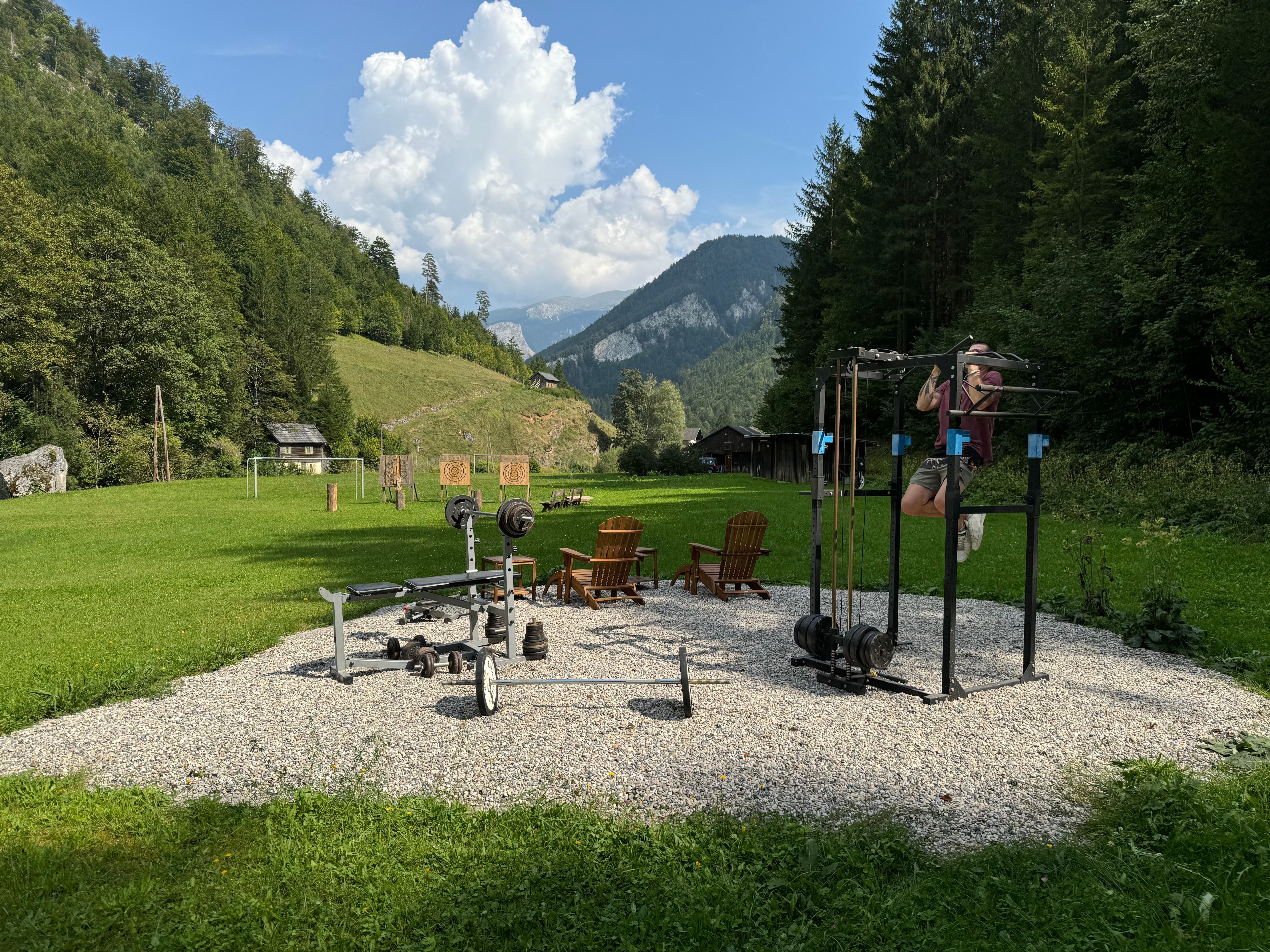 Outdoor fitness area with training equipment in a green, mountainous landscape.