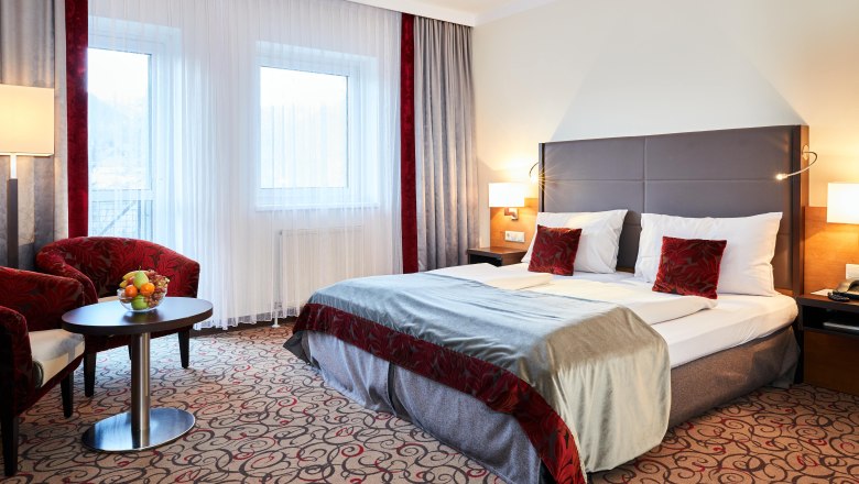 Double room at Hotel Schneeberghof with double bed, red pillows, table with fruit bowl and two armchairs.