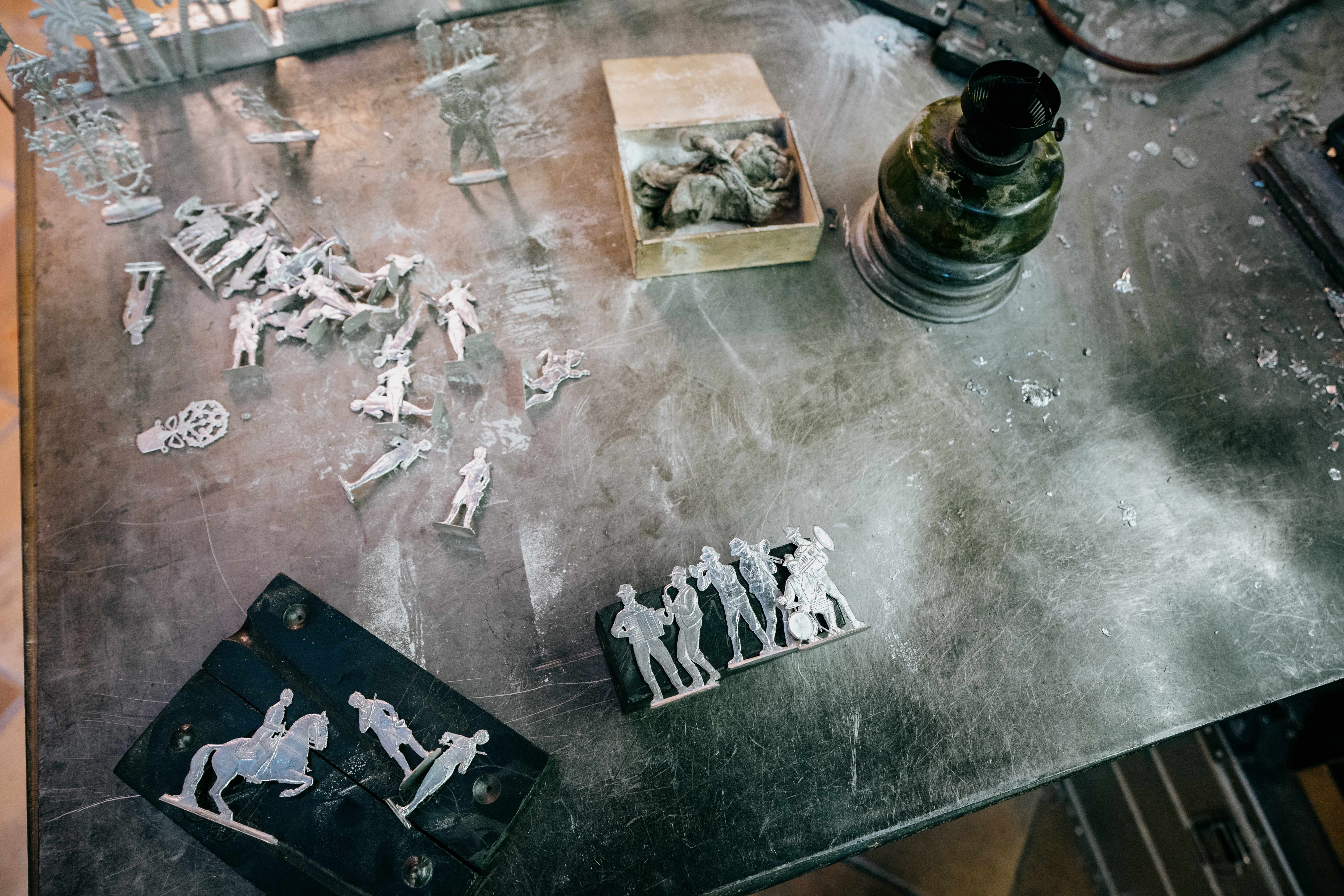 Unpainted pewter figurines on a table with tools and materials.
