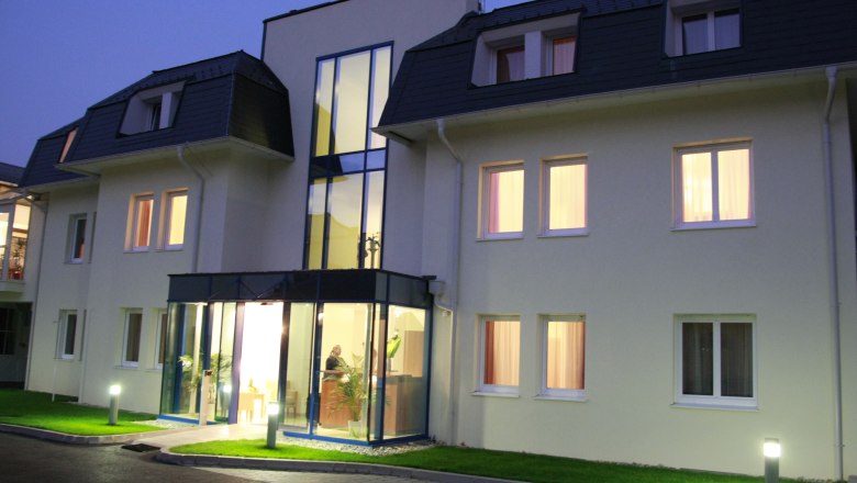 Entrance area of a modern hotel at dusk with illuminated windows and glass façade.