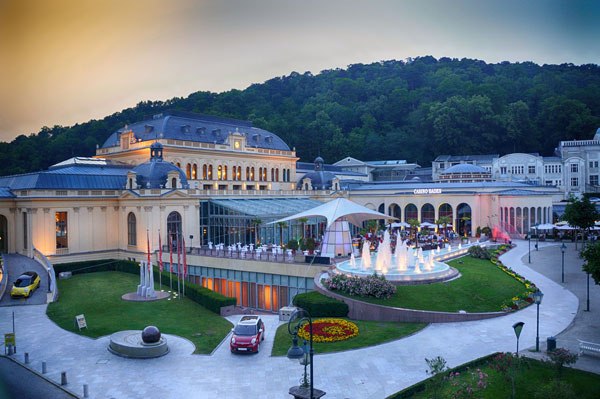 Exterior view of Casino Baden with illuminated fountain and surrounding green areas.