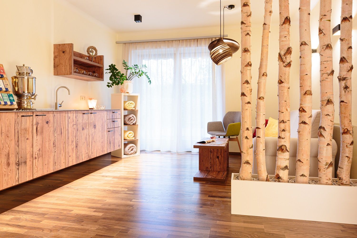 A cozy relaxation room with wooden furniture, plants and birch trunks as room dividers.
