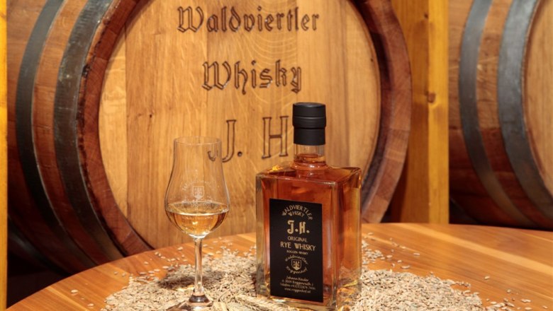 Bottle of Waldviertel whisky and glass on table with grain in front of wooden barrel.