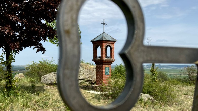 A small brick chapel with a cross on a hill, photographed through a heart-shaped metal grid.