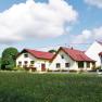 An organic farm with several yellow buildings and red roofs, surrounded by green meadows and trees under a blue sky with clouds.