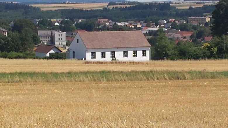Vacation home Peter, © Peter Schlager A white house with a red roof stands in a field, with a town and woods in the background.