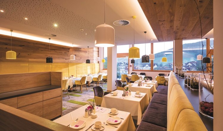 Restaurant with covered tables, benches and chairs, ceiling lamps and large windows.