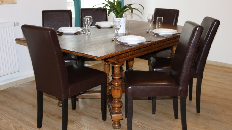 Dining area with wooden table and six brown chairs, set for six people.