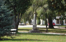 A small park with a stone monument and a bench surrounded by trees.