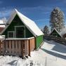 Snow-covered wooden huts in a wintry landscape with a blue sky.