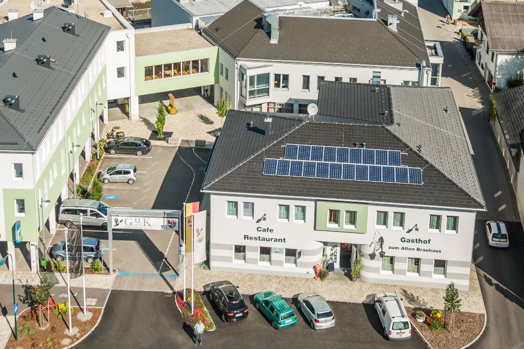 Aerial view of a building complex with the Gasthof zum Alten Brauhaus, solar panels on the roof and several parked cars.
