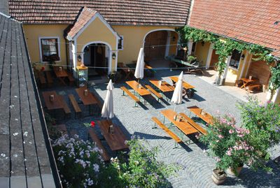 Inner courtyard of a Buschenschank (typical tavern) with wooden tables and parasols.