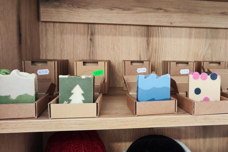 Handmade soaps in different colors and patterns on a wooden shelf.