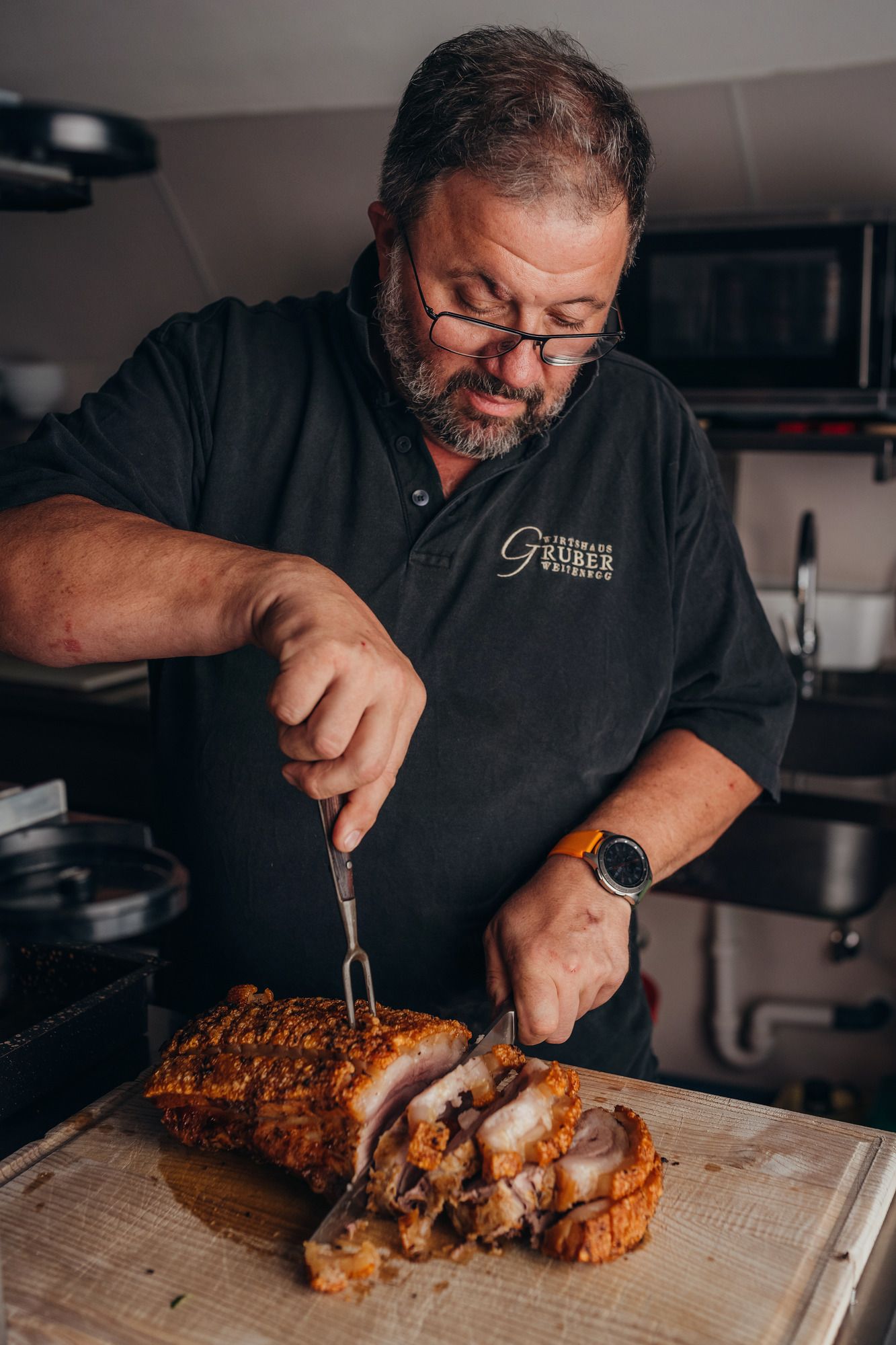 Man slicing crispy roast pork in a kitchen.