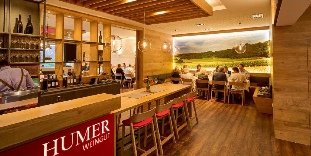 Interior view of a modern wine tavern with wooden furniture and a large photo wallpaper of a vineyard.