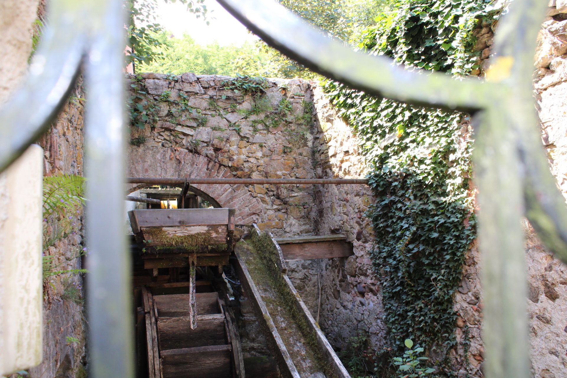 Detail of an old hammer mill with water wheel and ivy-covered stone walls.
