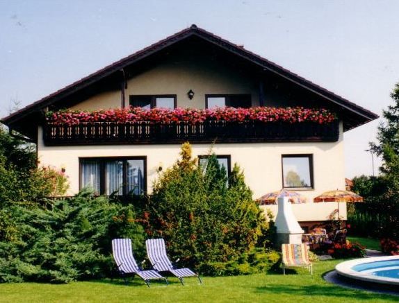 Two-storey house with balcony, garden furniture and pool in the foreground.