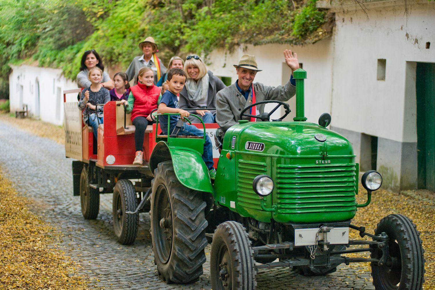 Green tractor with trailer full of people on a paved road.