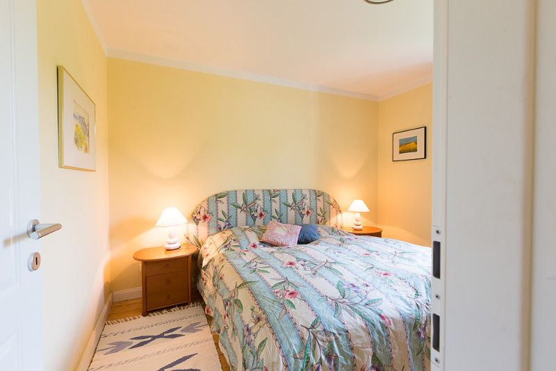 Cozy bedroom with double bed, floral comforter cover and two bedside tables with lamps. Yellow walls and pictures on the walls.