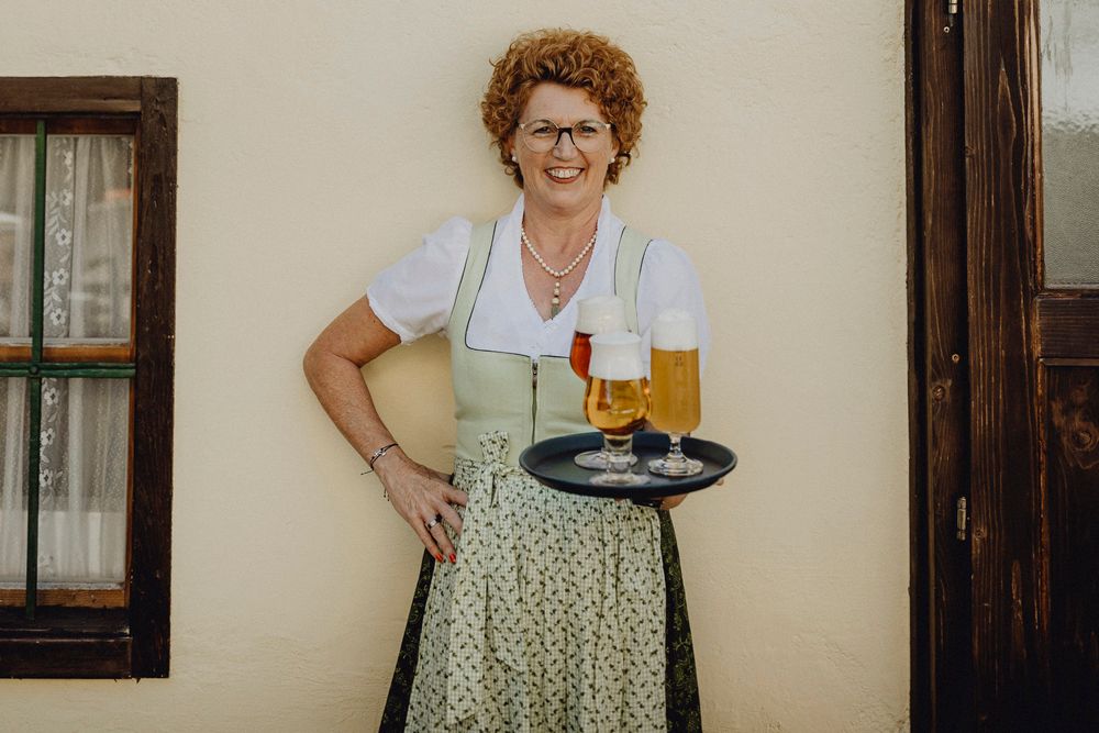 Woman in traditional dress with tray full of beer glasses in front of a wall.