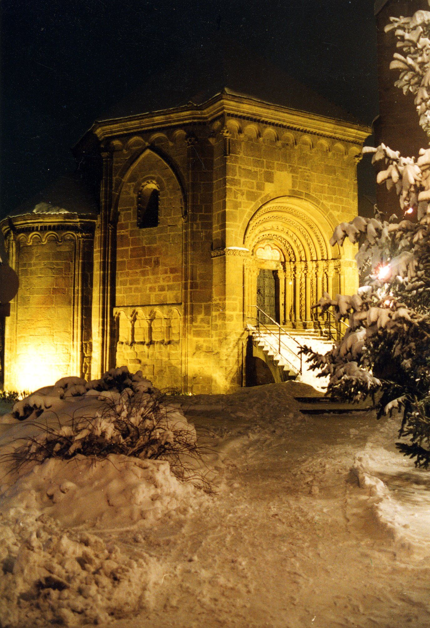 The Tulln charnel house at night, surrounded by snow, with illuminated Romanesque architecture.