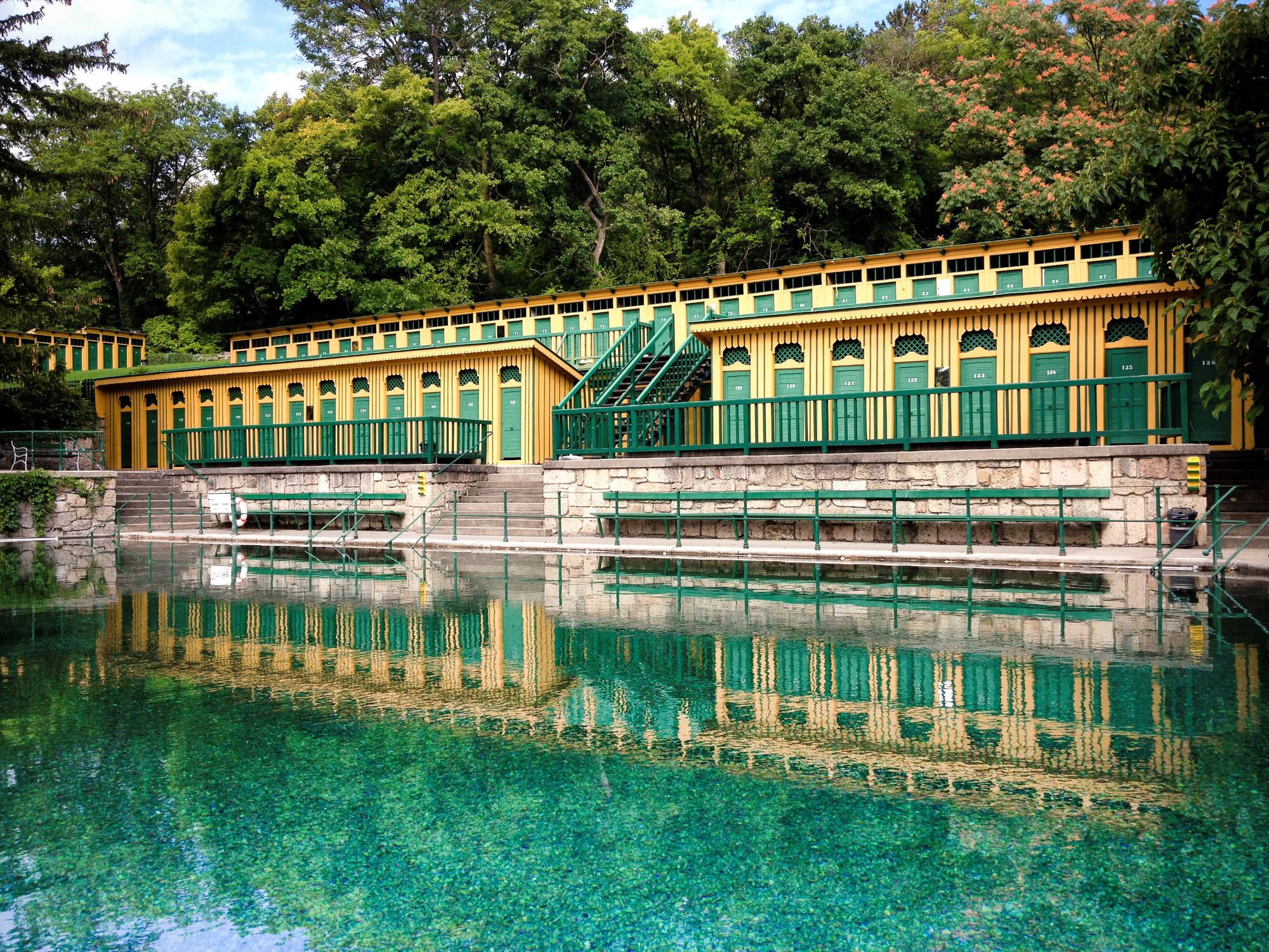 Historic bathhouse in Bad Fischau with green-yellow façade and reflecting water.