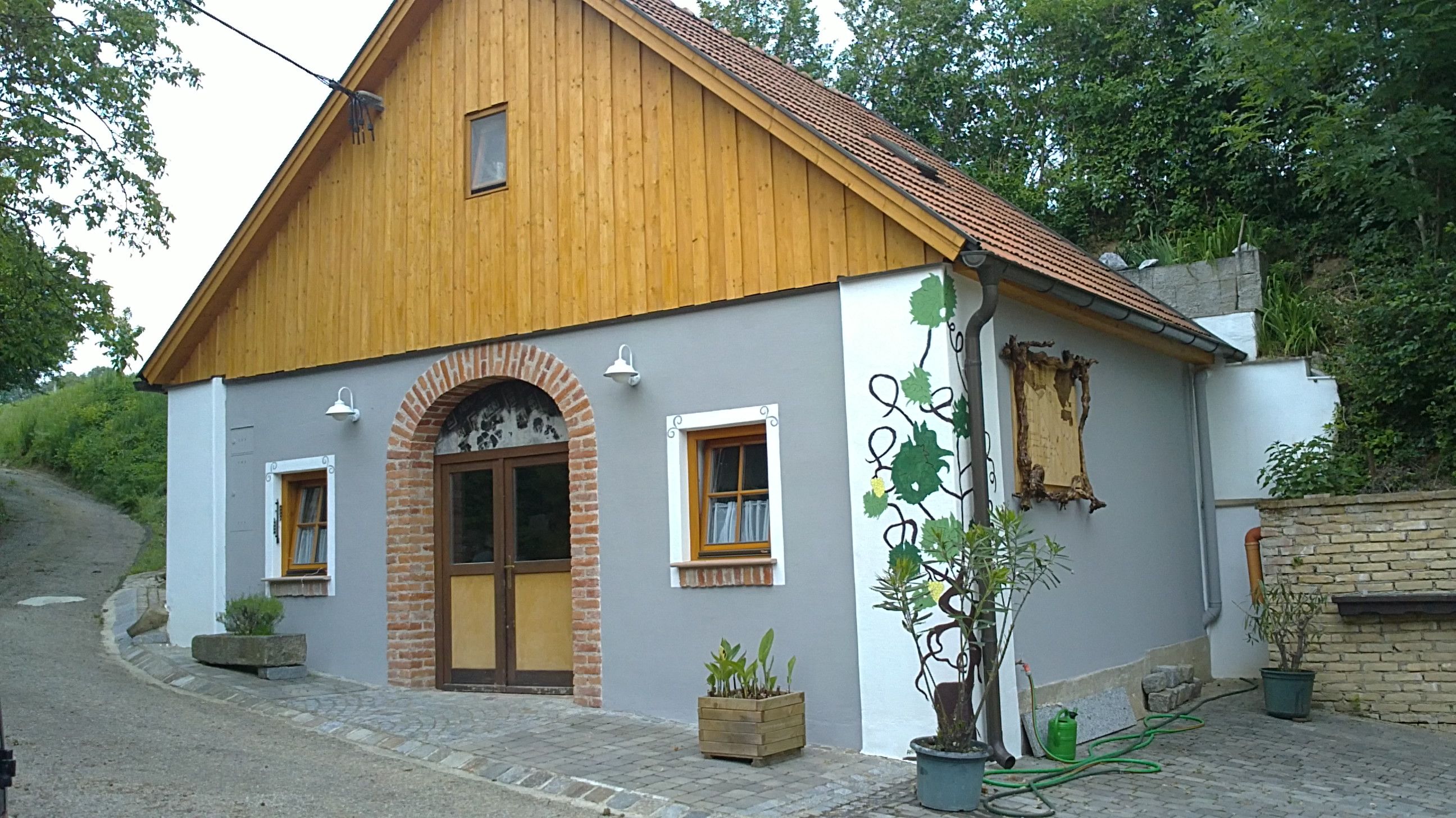 A traditional wine tavern with wooden cladding and brick arches, surrounded by plants.