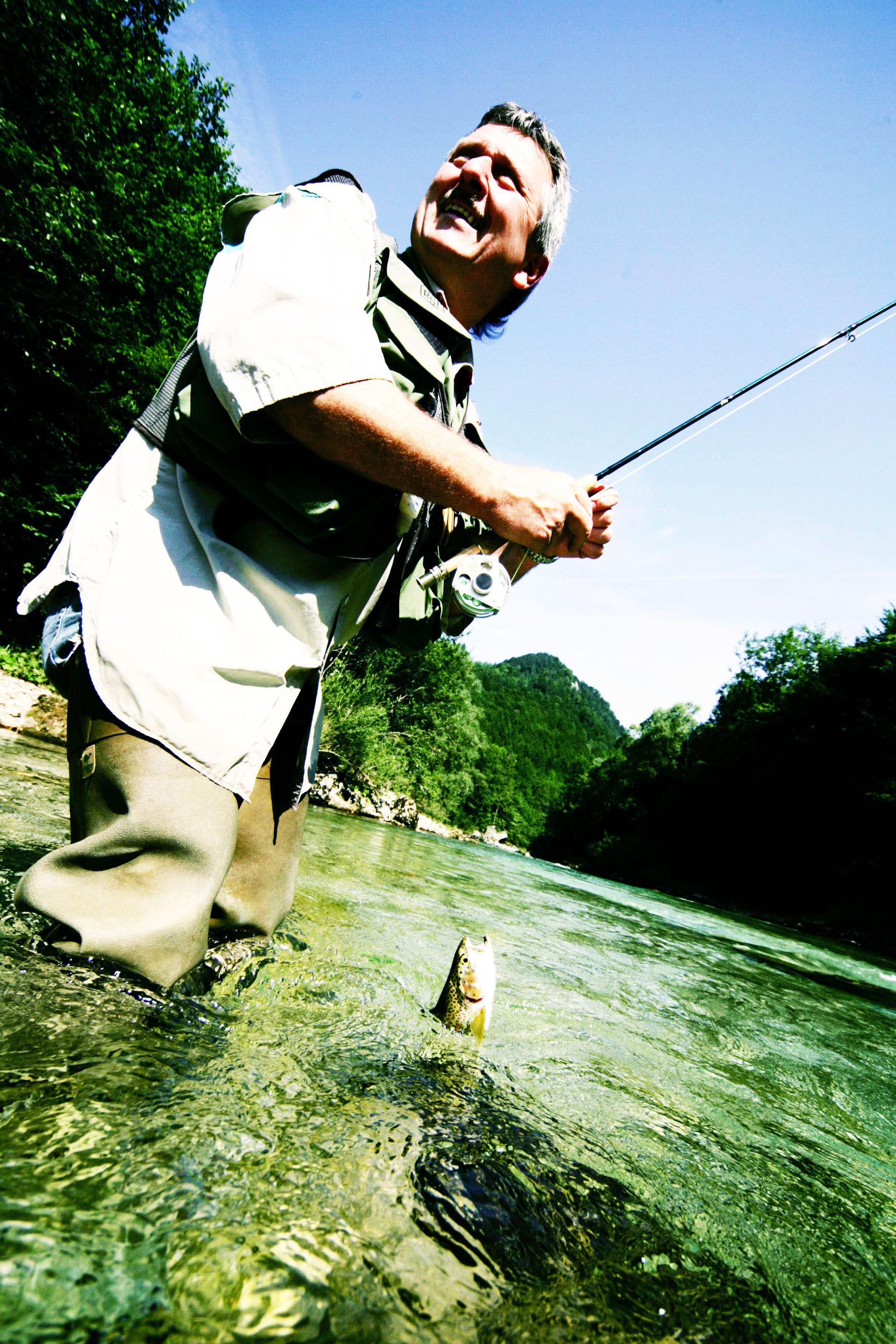 A man fly fishing in a river, with a jumping fish in the foreground.